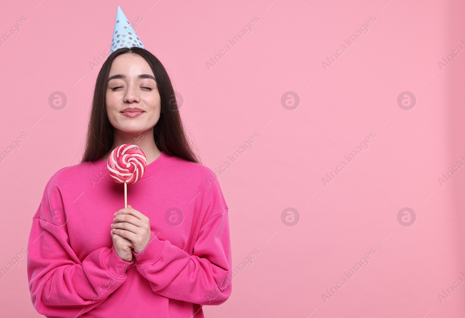 Photo of Woman in party hat holding lollipop on pink background, space for text