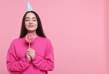 Woman in party hat holding lollipop on pink background, space for text