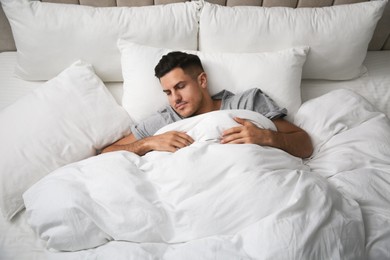 Photo of Handsome man sleeping under soft blanket in bed at home, above view