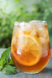 Photo of Delicious iced tea in glass on blue wooden table outdoors, closeup
