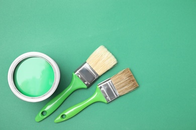 Photo of Open can with paint and brushes on green background, flat lay. Space for text