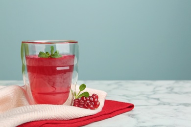 Glass of fruit jelly and pomegranate seeds on marble table, space for text