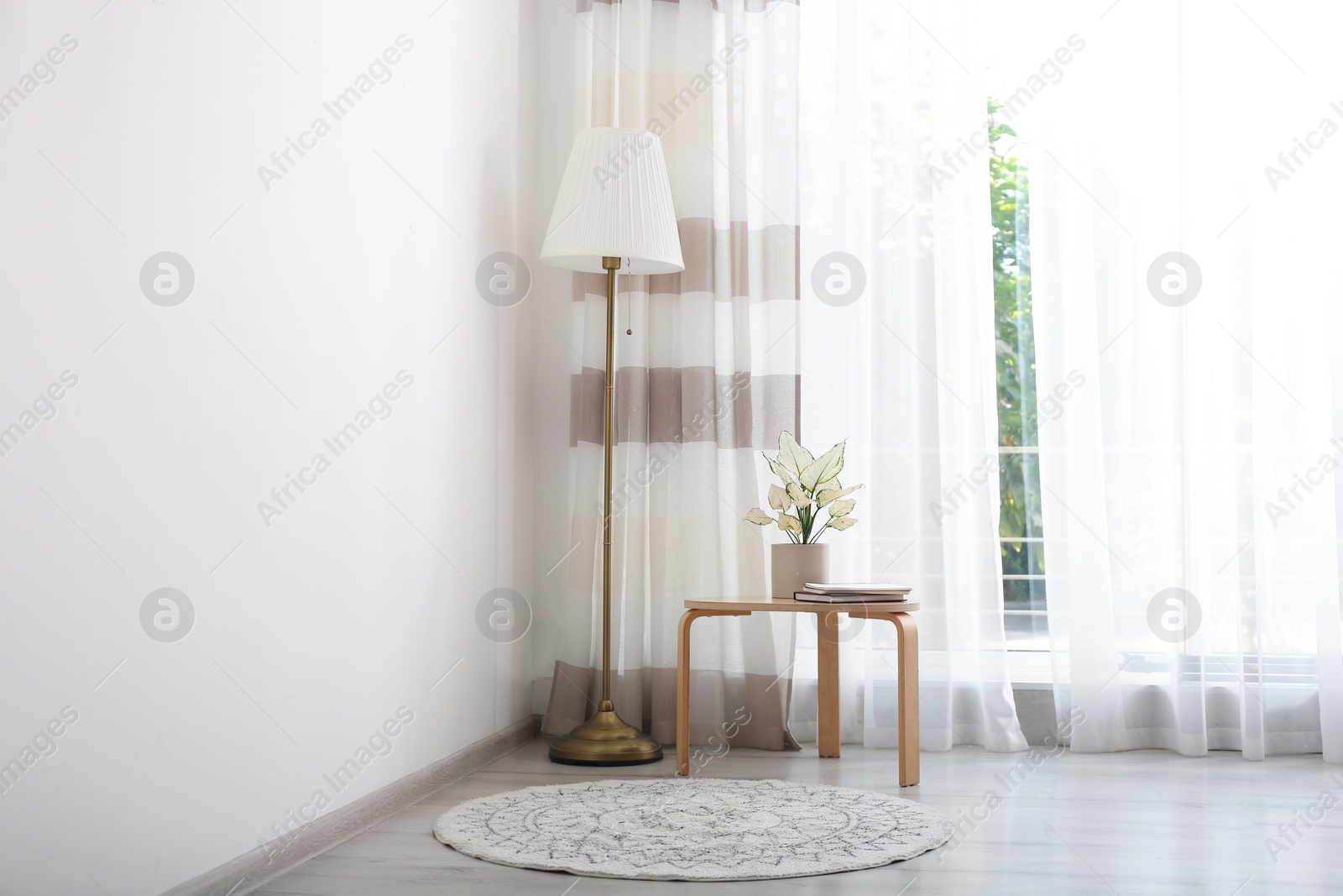 Photo of Small table and floor lamp near window with stylish curtains in living room. Interior design