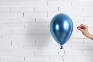 Photo of Young woman piercing bright balloon near brick wall, space for text