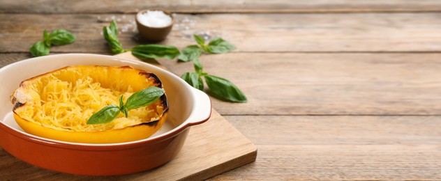 Image of Half of cooked spaghetti squash with basil in baking dish on wooden table. Banner design with space for text