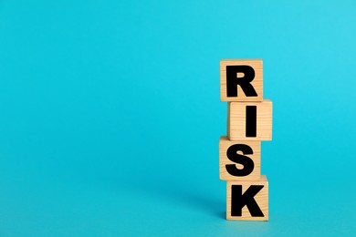 Photo of Word Risk made of wooden cubes on turquoise background, space for text