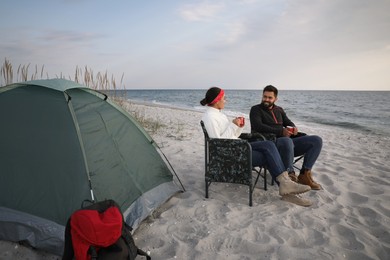 Photo of Couple with hot drinks near camping tent on beach