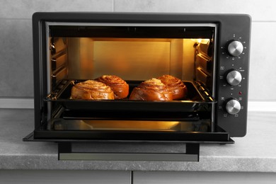 Photo of Open electric oven with delicious pastry on grey table indoors