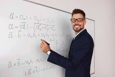 Happy teacher explaining mathematics at whiteboard in classroom