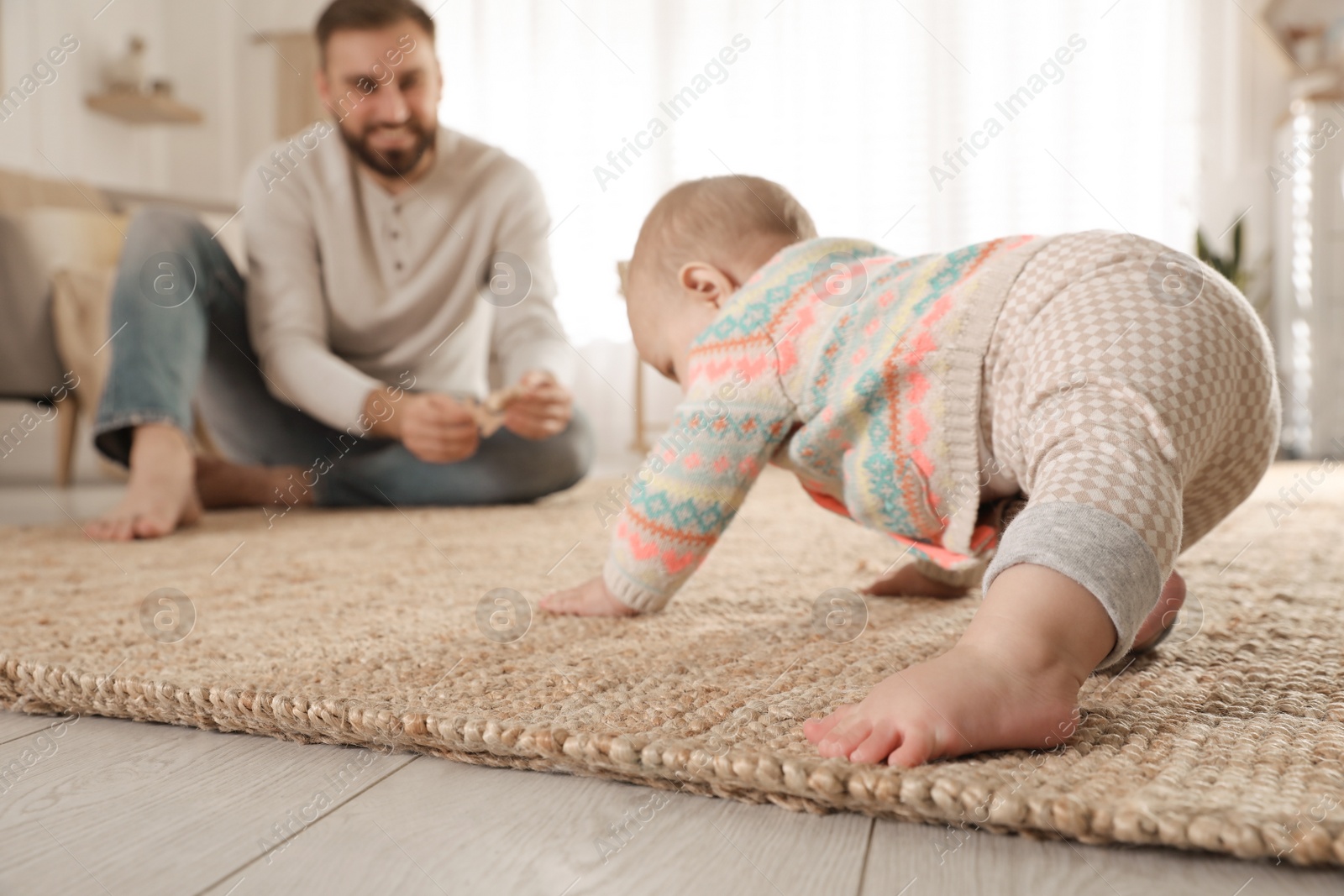 Photo of Happy young father watching his cute baby crawl on floor at home