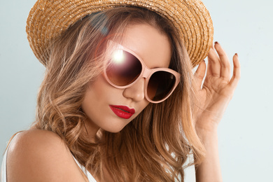 Image of Young woman wearing stylish sunglasses and hat on light grey background