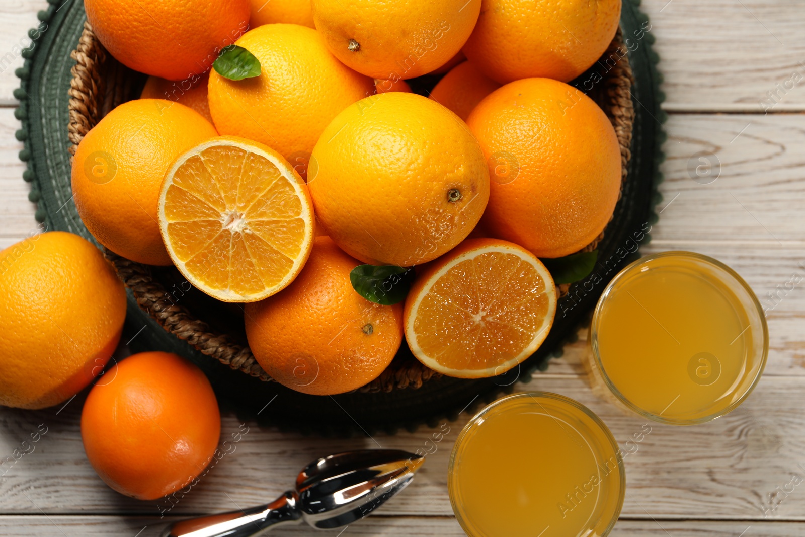 Photo of Many ripe juicy oranges, squeezer and fresh juice on white wooden table, flat lay