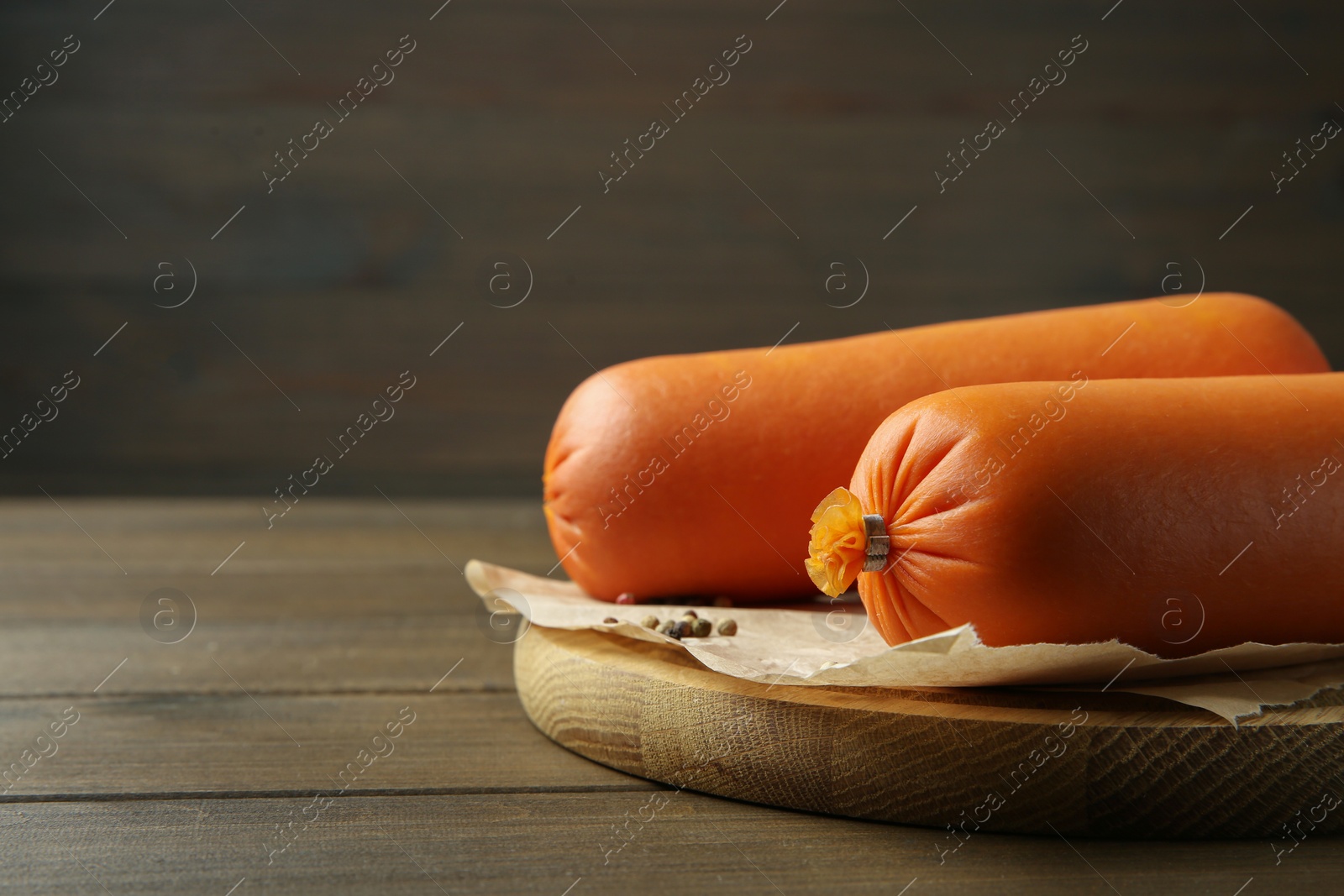 Photo of Board with tasty boiled sausages on wooden table, closeup. Space for text