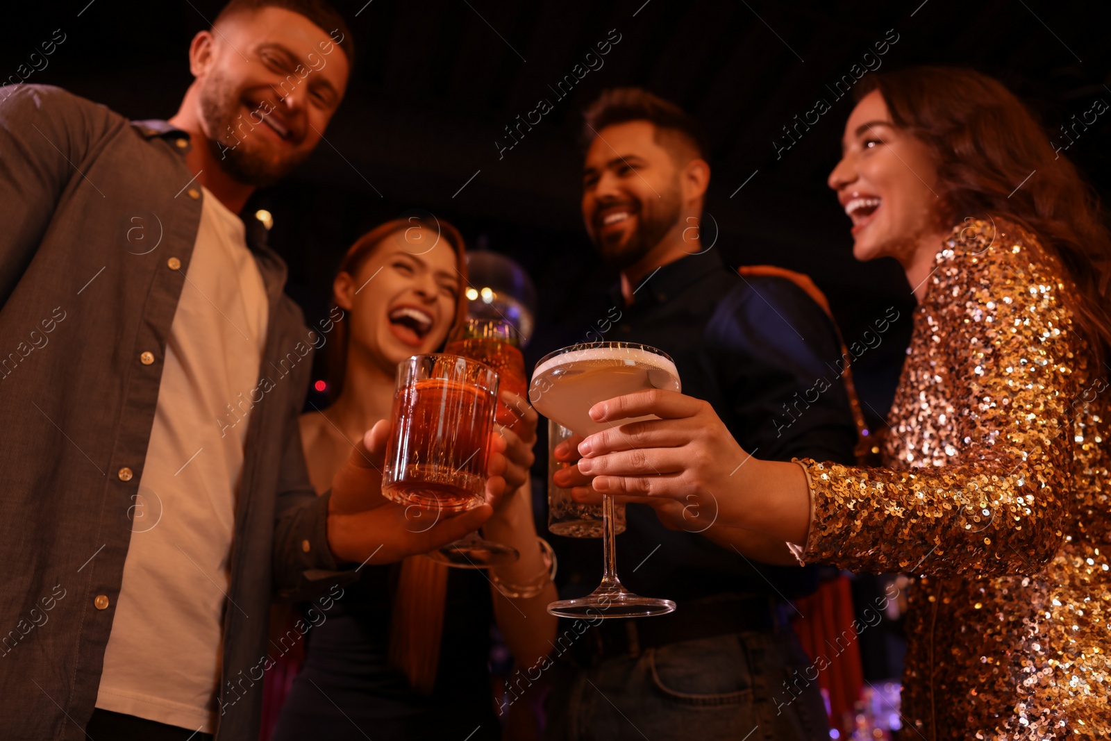 Photo of Happy friends clinking glasses with fresh cocktails in bar, low angle view