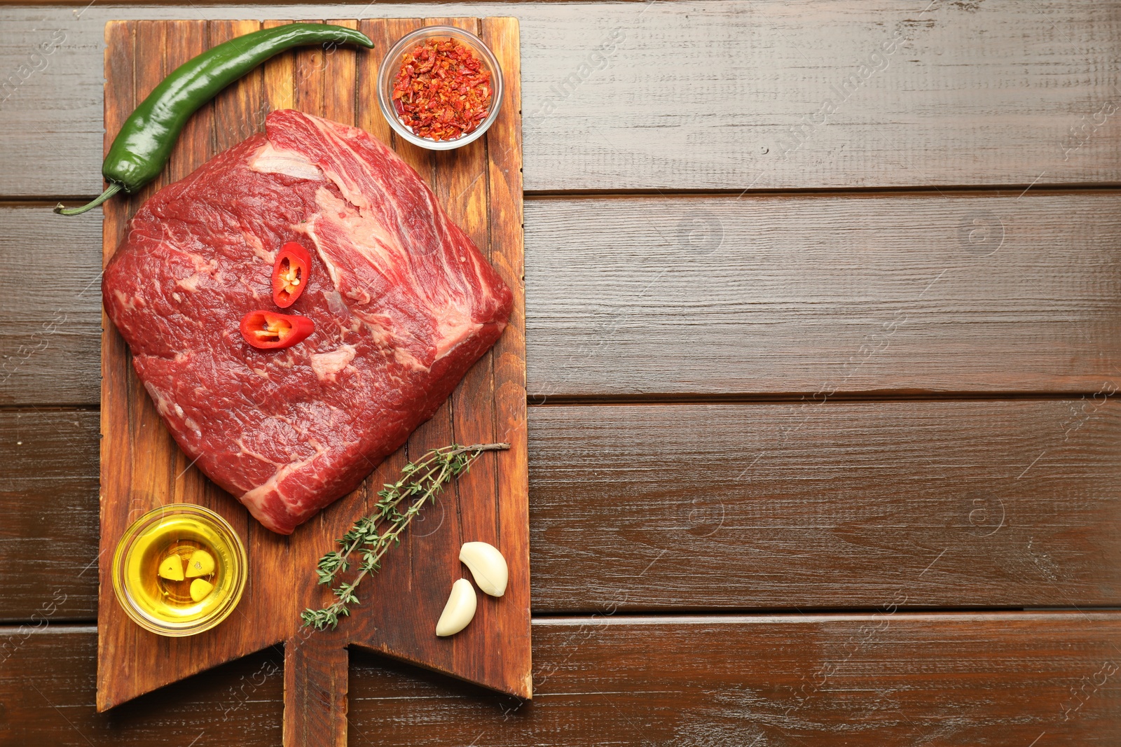 Photo of Fresh raw beef cut, spices and oil on wooden table, top view. Space for text