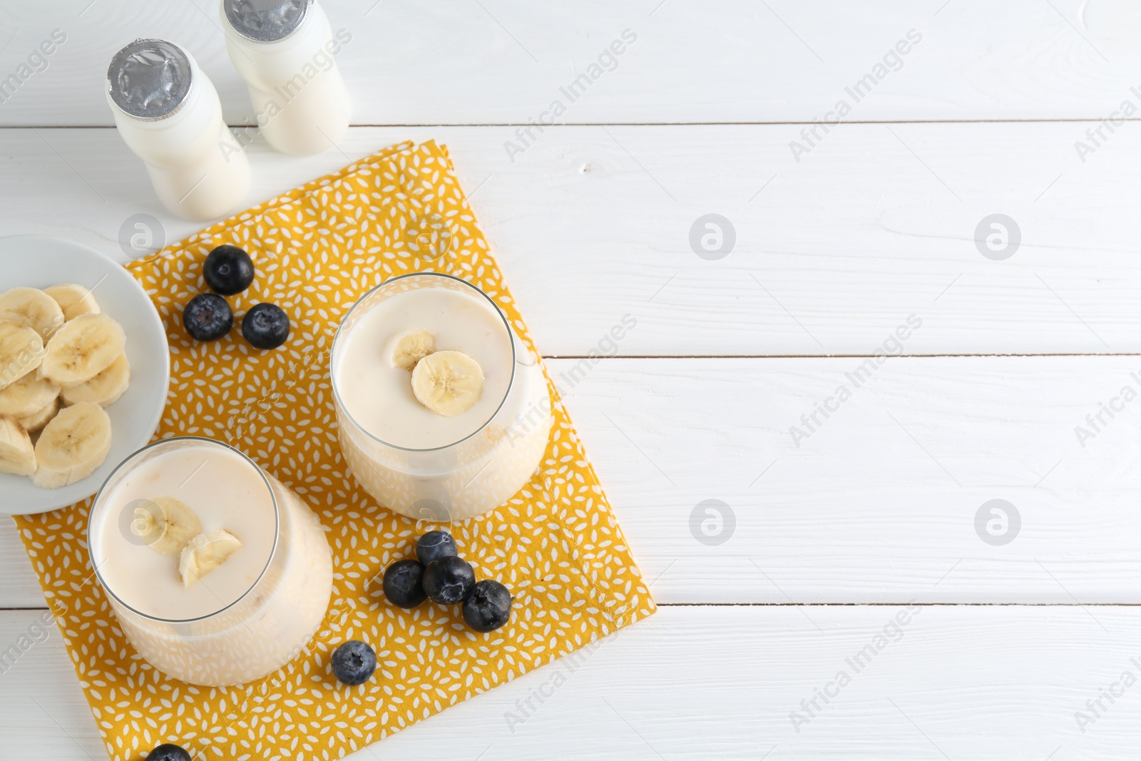 Photo of Tasty yogurt, banana and blueberries on white wooden table, top view. Space for text