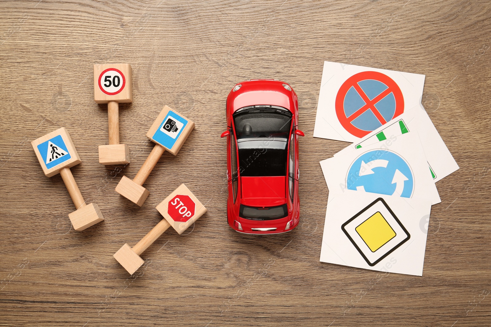 Photo of Many different road signs and toy car on wooden background, flat lay. Driving school