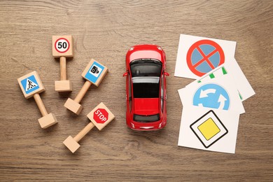 Many different road signs and toy car on wooden background, flat lay. Driving school