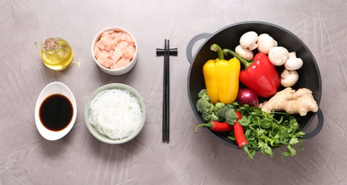 Photo of Wok, chopsticks and different products on grey textured table, flat lay