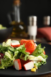 Photo of Delicious salad with crab sticks and lettuce on black plate, closeup