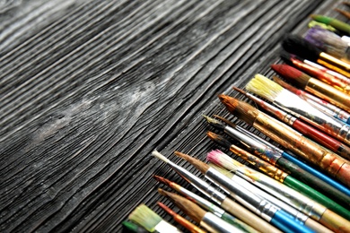 Photo of Different paint brushes on wooden table, closeup. Space for text