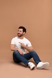 Smiling man pointing at something on light brown background