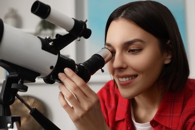 Photo of Beautiful young woman looking at stars through telescope in room, closeup