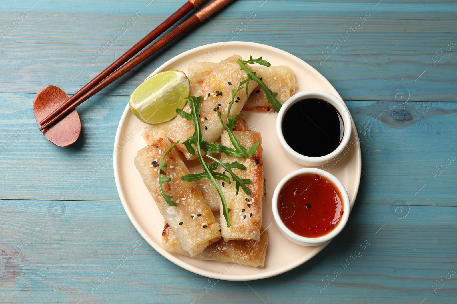 Photo of Tasty fried spring rolls served on light blue wooden table, flat lay