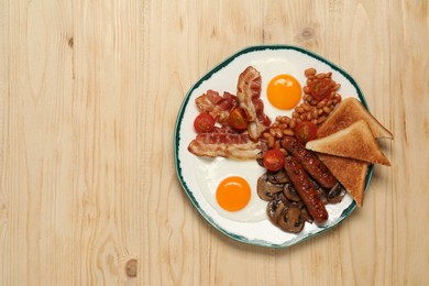 Photo of Plate of fried eggs, mushrooms, beans, bacon, sausages and toasts on wooden table, top view with space for text. Traditional English breakfast