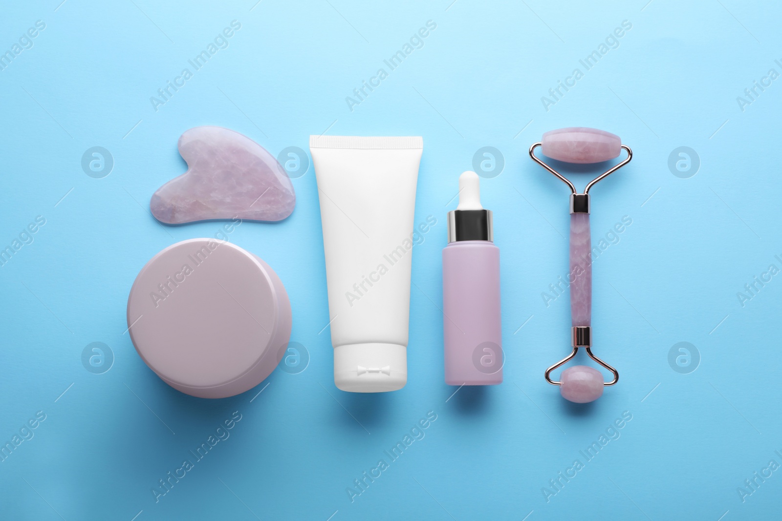 Photo of Natural face roller, gua sha tool and cosmetic products on light blue background, flat lay