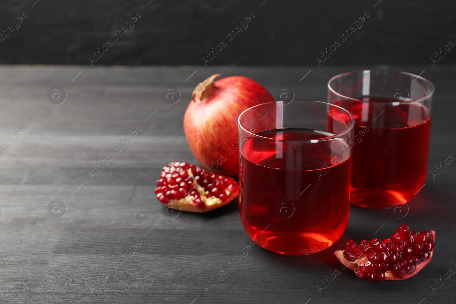 Photo of Tasty pomegranate juice in glasses and fresh fruits on black wooden table. Space for text