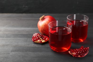 Photo of Tasty pomegranate juice in glasses and fresh fruits on black wooden table. Space for text