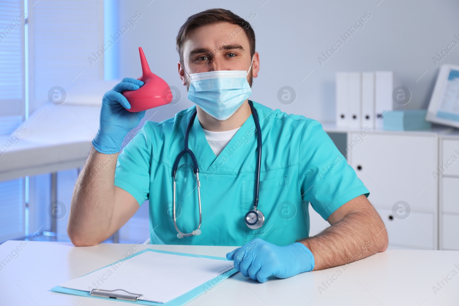 Photo of Doctor holding rubber enema at table in examination room