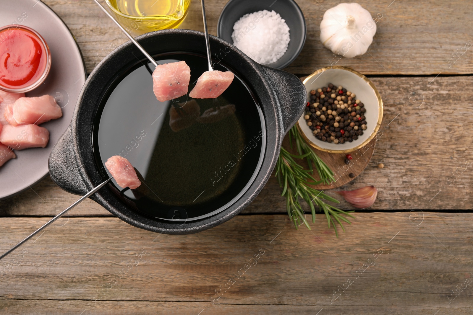 Photo of Fondue pot with oil, forks, raw meat pieces and other products on wooden table, flat lay. Space for text