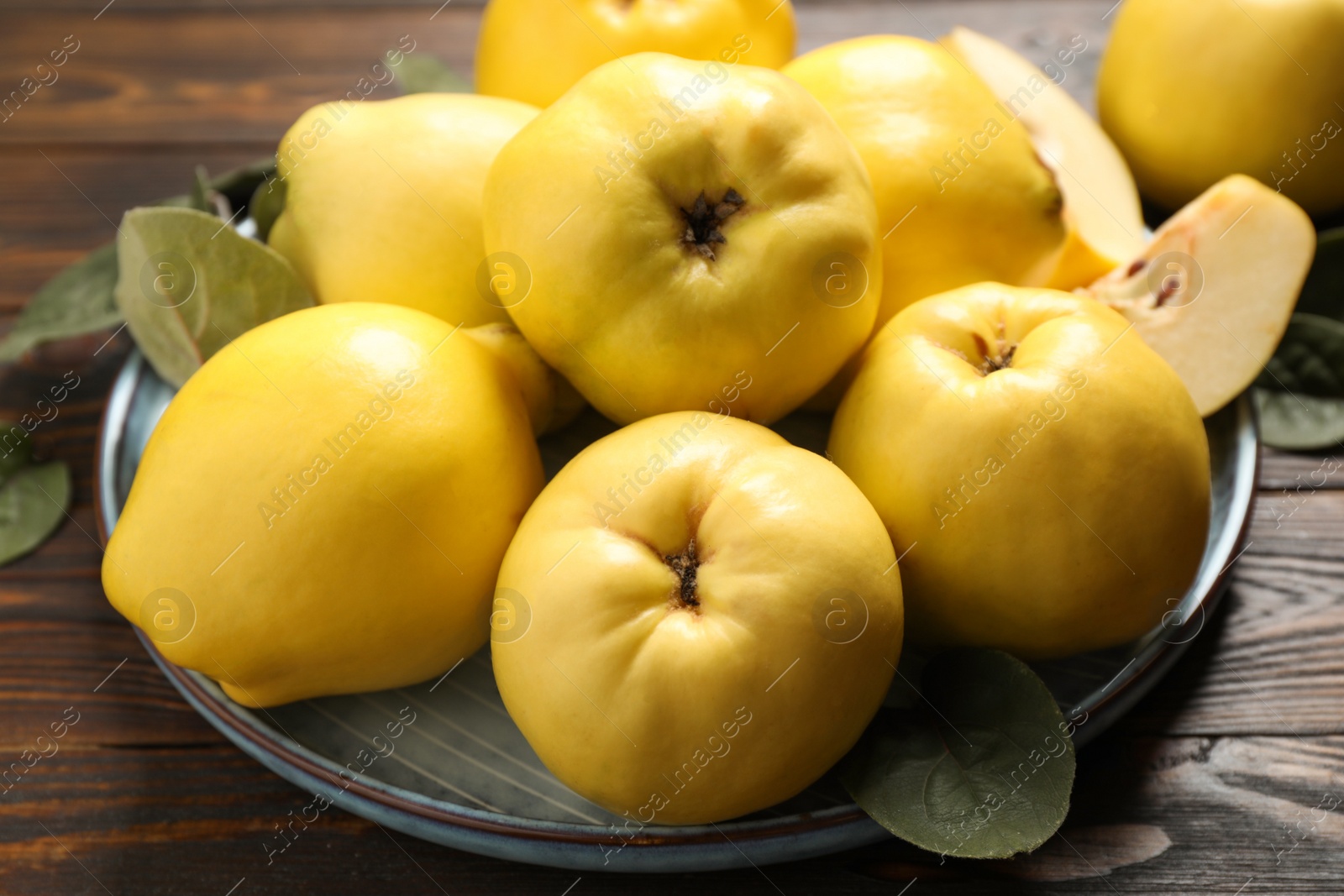 Photo of Fresh ripe organic quinces with leaves on wooden table, closeup