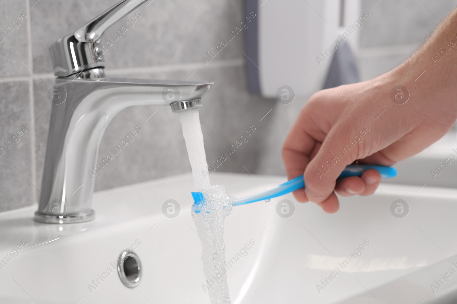 Photo of Man holding toothbrush under flowing water above sink in bathroom, closeup