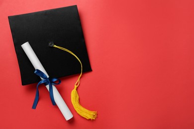 Photo of Graduation hat and diploma on red background, flat lay. Space for text