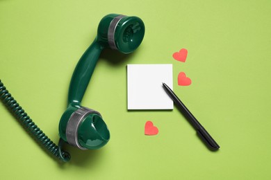 Photo of Long-distance relationship concept. Telephone receiver, empty note, paper hearts and pen on light green background, flat lay. Space for text