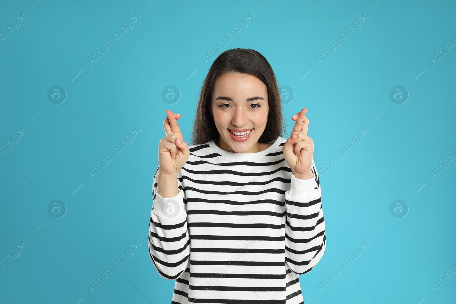 Photo of Woman with crossed fingers on light blue background. Superstition concept