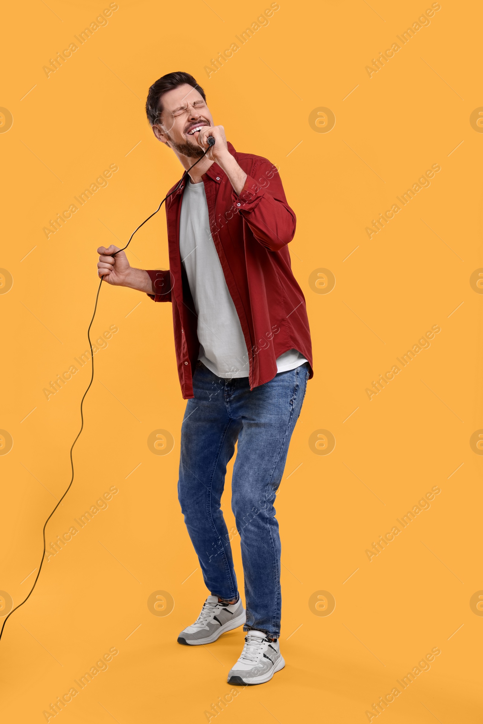 Photo of Handsome man with microphone singing on yellow background