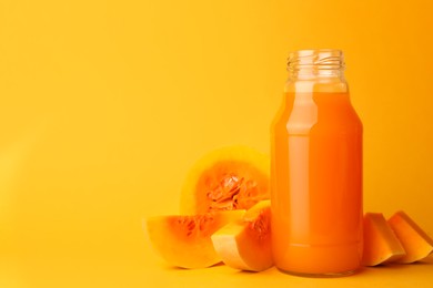 Photo of Tasty pumpkin juice in glass bottle and cut pumpkin on orange background. Space for text