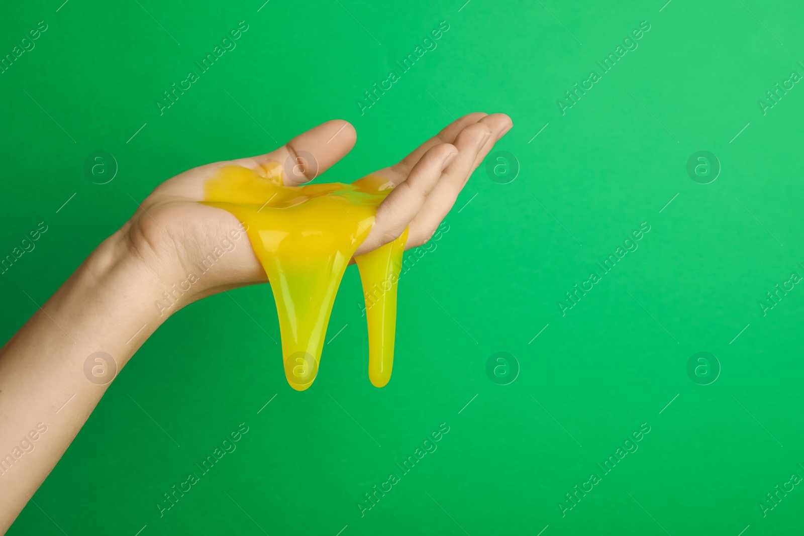 Photo of Woman playing with yellow slime on green background, closeup. Antistress toy
