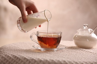Photo of Woman pouring milk into cup with aromatic tea at table, closeup