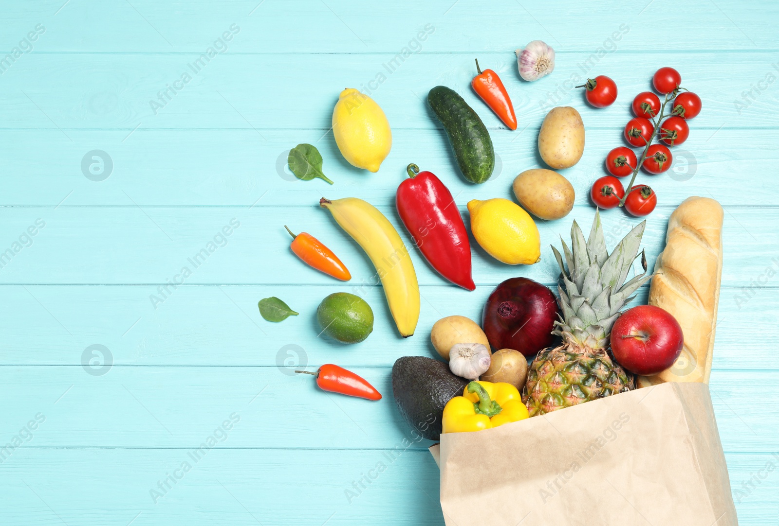 Photo of Shopping paper bag with different groceries on light blue wooden background, flat lay. Space for text