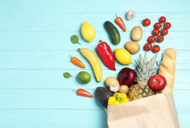 Shopping paper bag with different groceries on light blue wooden background, flat lay. Space for text