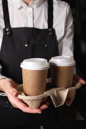 Photo of Barista holding takeaway paper cups with coffee in cafe, closeup