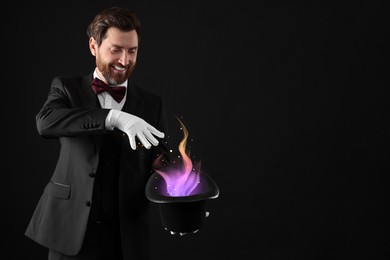 Magician showing trick with fantastic light coming out of top hat on dark background
