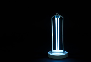 Photo of Modern ultraviolet lamp glowing on black background