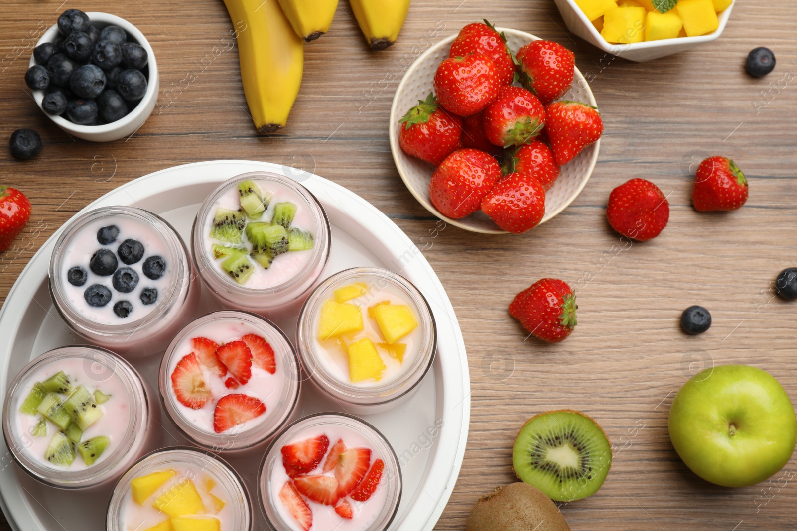 Photo of Yogurt maker with jars and different fruits on wooden table, flat lay