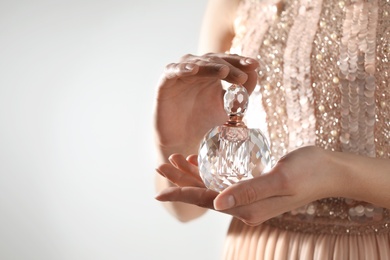 Photo of Young woman with bottle of perfume on light background, closeup. Space for text